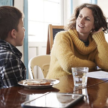 A mother and child sitting at the kitchen table, talking to each other about feelings surrounding chronic illness