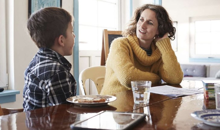 A mother and child sitting at the kitchen table, talking to each other about feelings surrounding chronic illness